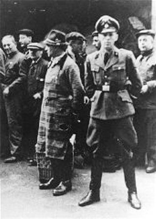 An SS officer stands in front of Jews assembled for deportation. Vienna, Austria, 1941